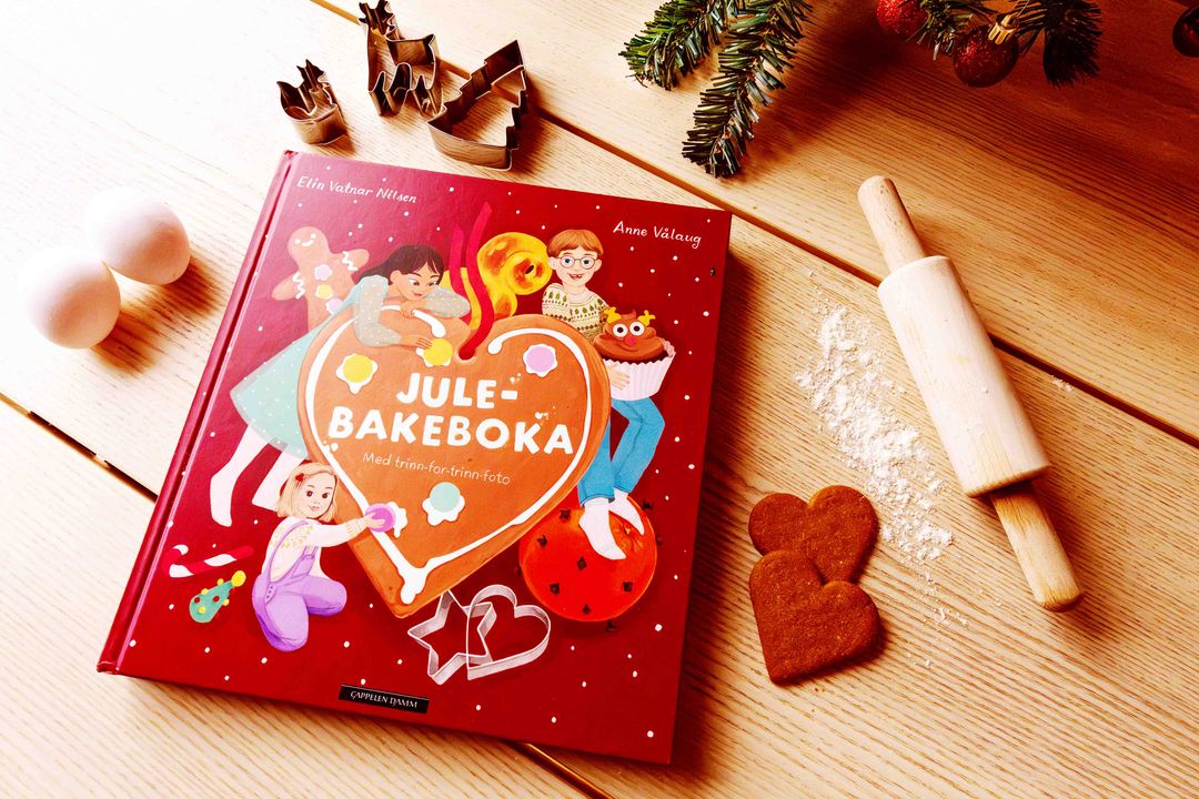 Omslaget på barneboken Julebakeboka - 2026 av Elin Vatnar Nilsen. Forsiden viser en fargerik og koselig illustrasjon av barn som baker julebakst på kjøkkenet, utgitt av Cappelen Damm.